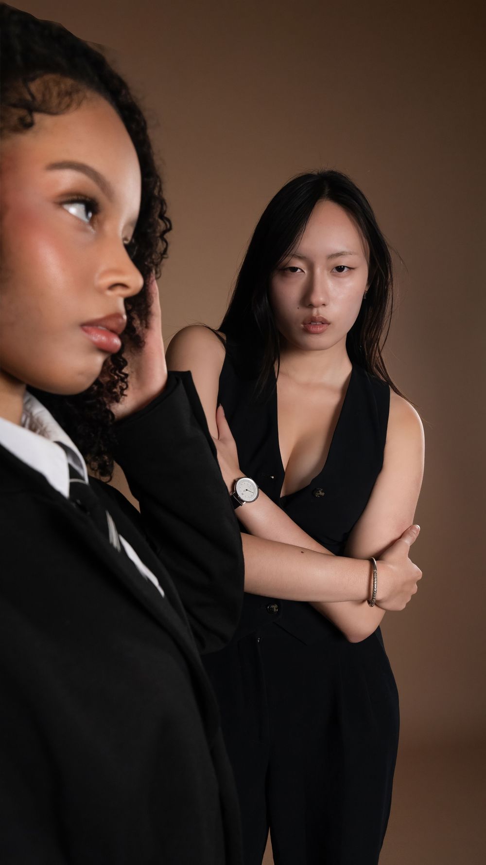 Two models in black photographed against a brown studio backdrop