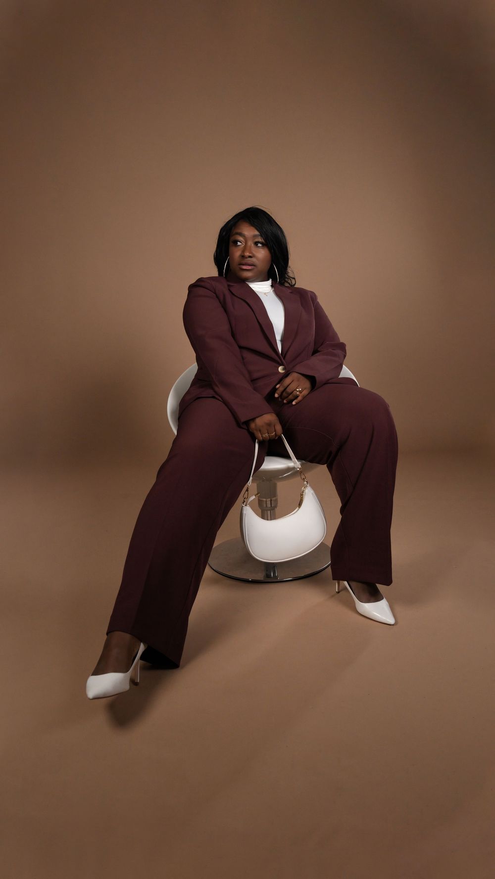 Seated fashion portrait in a burgundy suit with a white handbag