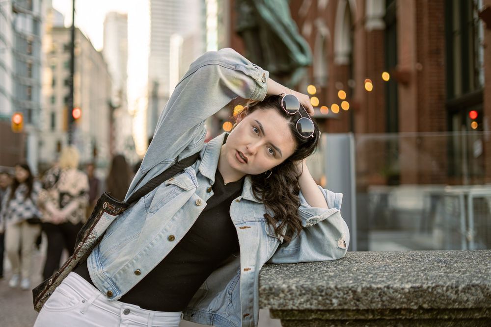 Model in a denim jacket leaning against a stone ledge